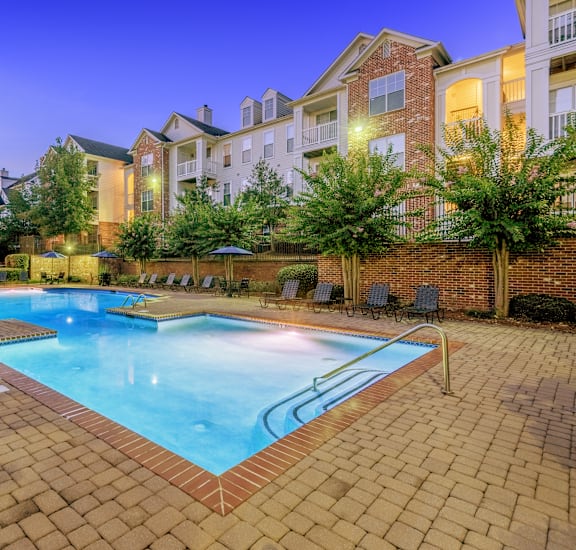 A swimming pool surrounded by a brick patio at dusk.